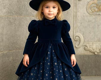 May include: A navy blue velvet witch costume for a child. The dress has a star-patterned skirt and a matching hat. The long-sleeved dress features a bow tie and a layered skirt with a tulle hem.