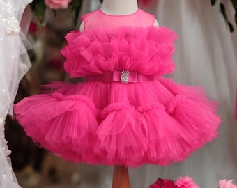 Puede incluir: Un vestido de tul rosa brillante con una falda con volantes y un lazo de satén con un adorno de pedrería en la cintura.