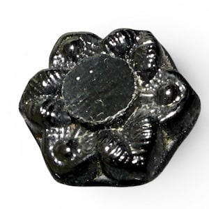 Può includere: Oggetto decorativo nero a forma di fiore con un centro circolare. L'oggetto ha una finitura lucida e una superficie strutturata dettagliata. I petali sono arrotondati e leggermente sovrapposti.