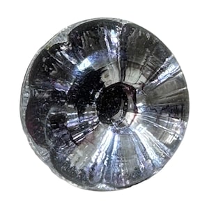 Può includere: Primo piano di un piccolo oggetto rotondo e metallico con un centro scuro. L'oggetto ha una superficie riflettente e strutturata con linee radiali che emanano dal centro. Il colore è principalmente argento con accenti grigio scuro e neri.