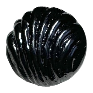 Può includere: Un bottone rotondo nero lucido caratterizzato da una superficie in rilievo e testurizzata con creste curve e radianti che imitano l'aspetto di una conchiglia. Il bottone presenta una finitura liscia e riflettente e una forma circolare.