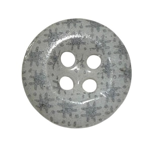 Può includere: Un bottone rotondo a quattro fori caratterizzato da una base color grigio chiaro con un motivo ripetuto di segni a forma di croce grigio scuro e piccoli punti distribuiti sull'intera superficie della chiusura.