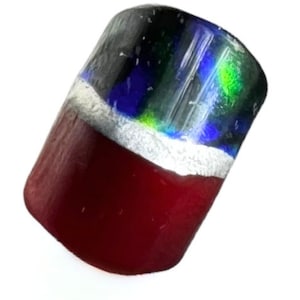 Può includere: Una perla di vetro cilindrica con una sfumatura di colore. La metà inferiore è rosso intenso, che sfuma in argento, poi in blu, verde e nero nella parte superiore. La perla è probabilmente per la creazione di gioielli.
