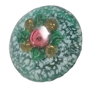 Può includere: Una perla di vetro rotonda e decorativa con un fiore rosa centrale circondato da foglie verdi e accenti dorati. La perla ha un aspetto strutturato e smerigliato con una combinazione di colori verde acqua e bianco.
