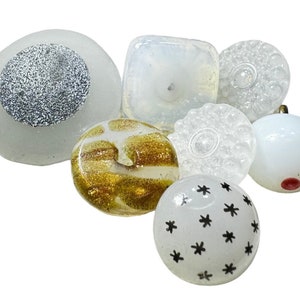 Può includere: Una collezione di pomelli decorativi in vetro di varie forme e design. I pomelli presentano una gamma di colori, tra cui bianco, oro e trasparente. Alcuni pomelli hanno accenti glitterati, mentre altri hanno disegni a motivi. Questi pomelli sono ideali per mobili o progetti artigianali.