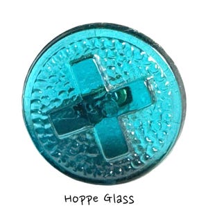 Può includere: Un bottone rotondo in vetro turchese con un disegno a croce al centro. Il bottone ha una superficie strutturata. Il testo "Hoppe Glass" è scritto sotto il bottone.