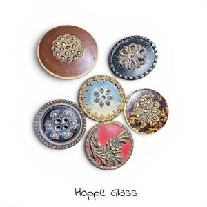 May include: A collection of six decorative buttons in various colors and designs. The buttons feature ornate patterns, including floral and geometric motifs, with metallic and jewel accents. The text "Hoppe Glass" is at the bottom.