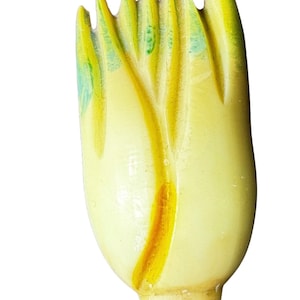 May include: A carved wooden hair comb featuring a stylized tulip bud shape. The object is primarily pale yellow with subtle green accents on the upper petal tips and a deeper yellow vertical groove running down the center of the main body.