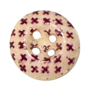 May include: A round, cream-colored button featuring a repeating pattern of small, dark purple cross-stitch style markings across its surface. The button has four circular holes positioned in the center for attachment to fabric or garments.
