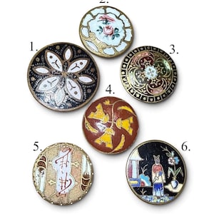 May include: Six round decorative buttons labelled 1 to 6. Button 1 is black with white petals. Button 2 is white with pink roses. Button 3 is gold with stars. Button 4 is rust with yellow flowers. Button 5 is beige with abstract lines. Button 6 is black with a figure.