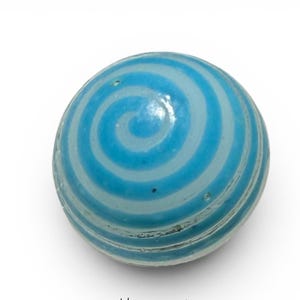 Può includere: Una biglia di vetro blu e bianca con spirali. La biglia presenta un design a spirale con bande alternate di azzurro e bianco. Il vetro ha una superficie leggermente strutturata e una finitura lucida. Questo giocattolo è un classico.