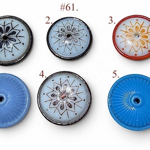 Peut inclure: Six boutons ronds étiquetés #61, disposés sur deux rangées. Quatre boutons présentent un centre blanc avec un motif en étoile noir ou orange et un bord foncé. Deux boutons sont bleu uni avec une texture nervurée et un trou central.