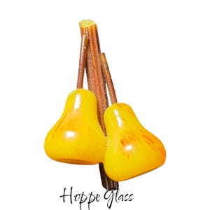 May include: Two yellow glass pears with brown stems, attached to a wooden branch. The pears have a glossy finish and are slightly textured.