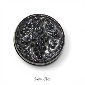 May include: A round, dark gray glass button with a raised grape and leaf design. The button has a textured edge and the words "Hoppe Glass" are printed at the bottom.