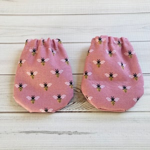 May include: Two pink fabric pouches with a bee pattern. The pouches have a drawstring closure.