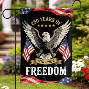 Op de afbeelding: Een zwarte tuin vlag met een Amerikaanse zeearend die twee Amerikaanse vlaggen vasthoudt. De vlag toont de tekst "250 YEARS OF FREEDOM 1776-2026" met sterren en strepen. De vlag is in een tuin.