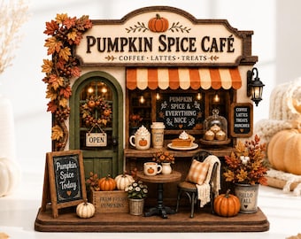 May include: A miniature Pumpkin Spice Café model featuring a green door, orange striped awning, and autumn foliage. The sign reads PUMPKIN SPICE CAFÉ, COFFEE, LATTES, TREATS. Includes a chalkboard sign, small pumpkins, a table, chair, and coffee cups.