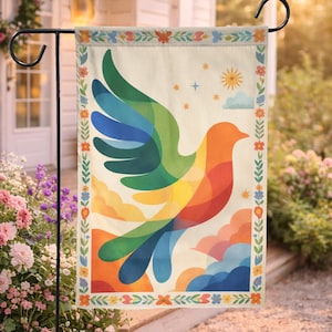 Puede incluir: Bandera de jardín decorativa con un diseño de paloma colorida. La paloma está representada con alas y cuerpo de colores del arcoíris, sobre un fondo crema con detalles florales y de nubes. La bandera se muestra en un soporte de metal negro.