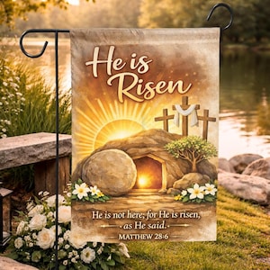 Könnte beinhalten: Eine Gartenflagge mit dem Text "He is Risen" und einer Darstellung des leeren Grabes mit Sonnenaufgang. Die Flagge enthält auch den Bibelvers Matthäus 28:6.