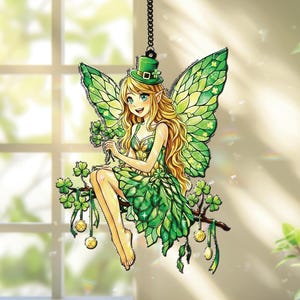 Pode incluir: Decoração suspensa com tema do Dia de São Patrício, apresentando uma fada com asas verdes, um vestido verde e um chapéu verde. A fada está sentada em um galho com trevos e moedas de ouro. O fundo inclui uma janela e luz natural.