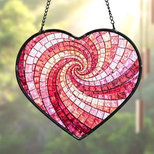 May include: A heart-shaped stained glass suncatcher with a spiral design. The mosaic pattern features shades of red, pink, and white, framed by a black metal border. It hangs from a black chain, perfect for window decor.
