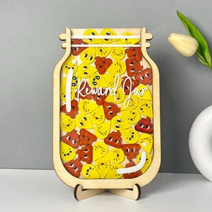 May include: Wooden reward jar with a clear front panel filled with yellow and orange poop emoji-shaped tokens. The jar has a white inscription that reads "Reward Jar".