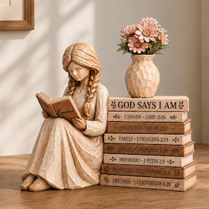 Peut inclure: Une figurine en résine beige représentant une fille aux cheveux tressés lisant un livre marqué Emma, assise à côté d'une pile de sept livres avec des textes religieux et un petit vase contenant des fleurs roses. Les livres portent les titres God Says I Am, Chosen, Protected, Family, Special, Important, Treasured et Precious.