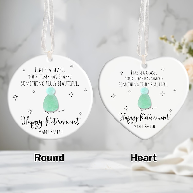 May include: Two white ceramic retirement ornaments, one round and one heart-shaped, with a ribbon for hanging. Each features a sea glass design and the text "Happy Retirement" with a name. The round ornament is labeled "Round", and the heart-shaped one is labeled "Heart".