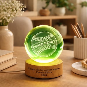 May include: A glowing green baseball-themed crystal ball with the words "COACH HENRY" etched on the front. The ball sits on a wooden base with the text "Thank you for a great season Fireball Flyers 2026".