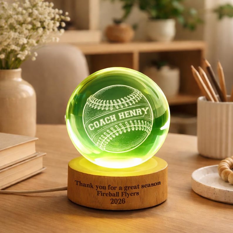 May include: A glowing green baseball-themed crystal ball with the words "COACH HENRY" etched on the front. The ball sits on a wooden base with the text "Thank you for a great season Fireball Flyers 2026".