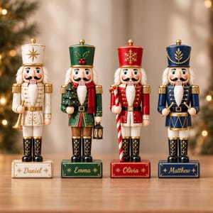 Può includere: Quattro statuette decorative di schiaccianoci allineate. Il primo è bianco con dettagli dorati, il secondo verde con un albero e una lanterna, il terzo rosso con un bastoncino di zucchero e il quarto blu con un tamburo. Ogni base è personalizzata con i nomi Daniel, Emma, Olivia e Matthew.