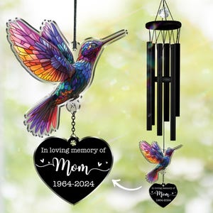 May include: A colorful hummingbird wind chime with a heart-shaped memorial. The hummingbird has a stained-glass effect with purple, orange, and blue hues. The heart reads "In loving memory of Mom 1964-2024". The wind chime has black tubes.