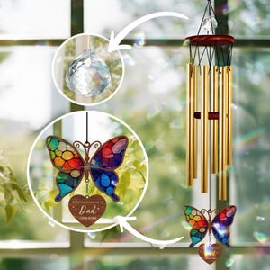 Pode incluir: Um carrilhão de vento em forma de borboleta de vidro colorido com um coração de madeira que diz "In loving memory of Dad 1964-2024". O carrilhão tem um prisma de cristal pendurado na parte inferior.