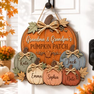 May include: A wooden door sign shaped like a large orange pumpkin with the text Grandma & Grandpa's PUMPKIN PATCH. It features five smaller pumpkins in green, cream, pink, blue, and orange, each with a raffia bow and the names Kate, Emma, Sophia, Nate, and Jack.