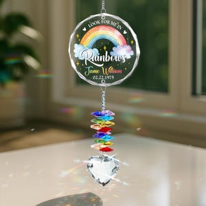 May include: A crystal suncatcher with a round, clear glass ornament featuring a rainbow and the text "Look for me in rainbows Jane William 02.22.1975". The ornament is hanging from a silver chain with a crystal heart and a rainbow of crystal beads.
