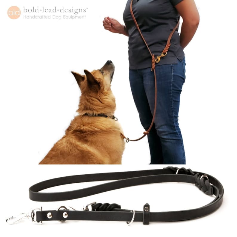 a black leather leash is shown both on a white background and with a person who wears the leash over-the-shoulder cross body. The person has one hand behind their back. The leash is attached to a sable dog who looks up at the person.