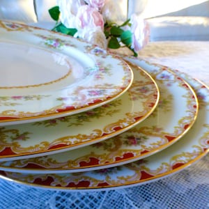 May include: Four white porcelain dinner plates with a gold and red floral pattern. The plates are stacked on top of each other.