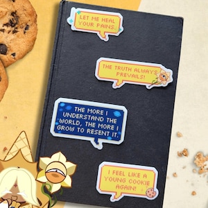 Puede incluir: Cuatro pegatinas de citas coloridas en un libro oscuro. Las pegatinas tienen diseños de bocadillos pixelados con frases como "Déjame curar tus dolores" y "¡La verdad siempre prevalece!" Temática de galletas.