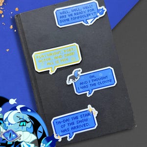 Pode incluir: Uma coleção de autocolantes coloridos em forma de balões de fala com várias frases, incluindo "Bem, bem, bem! Estamos prontos para alguma palhaçada?" e "Ta-da! A estrela do show chegou". Os autocolantes estão numa superfície escura.