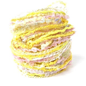 May include: A vibrant skein of yarn, predominantly yellow with strands of pink, white, and silver. The yarn is tightly wound, showcasing a textured, multi-colored design. Ideal for knitting or crochet projects.