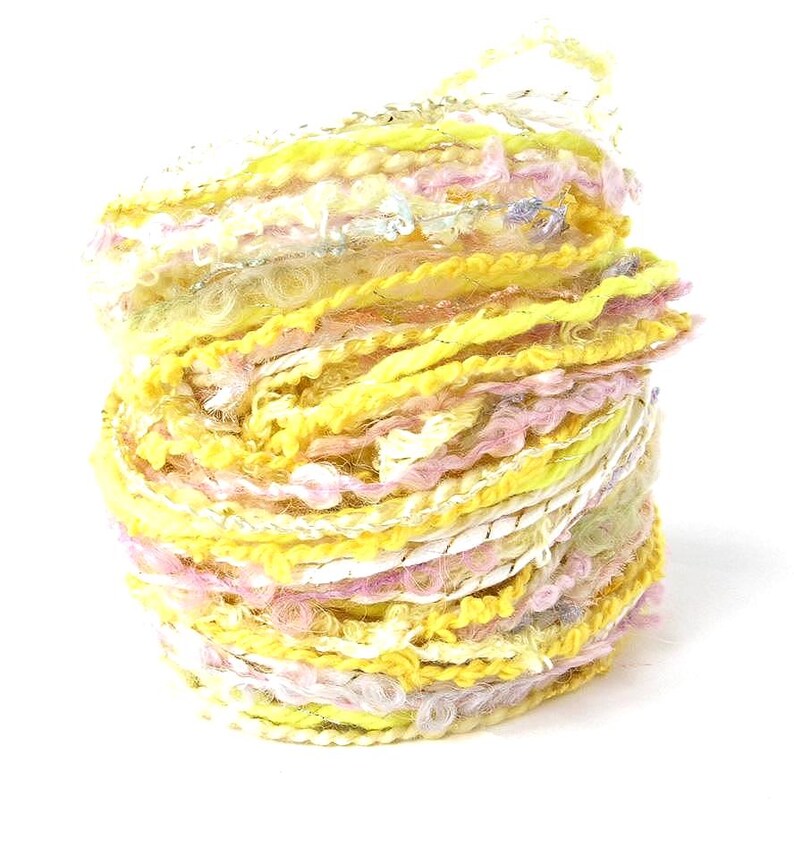 May include: A vibrant skein of yarn, predominantly yellow with strands of pink, white, and silver. The yarn is tightly wound, showcasing a textured, multi-colored design. Ideal for knitting or crochet projects.