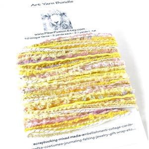 May include: Art yarn bundle featuring a mix of yellow, pink, and white yarns. The bundle includes 10 unique yarns, each 2 yards long, for a total of 20 yards. The yarn is suitable for scrapbooking, mixed media, and various crafts.