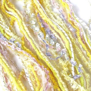 May include: Close-up of a collection of colorful yarn strands. The yarn features a mix of yellow, white, pink, and blue hues, with some strands having a textured, fuzzy appearance. The yarn is likely for crafting projects.