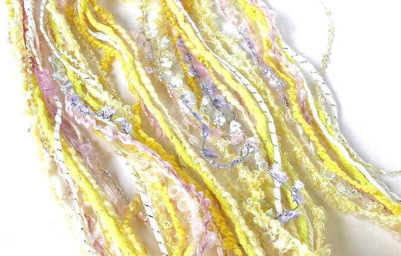 May include: Close-up of a collection of colorful yarn strands. The yarn features a mix of yellow, white, pink, and blue hues, with some strands having a textured, fuzzy appearance. The yarn is likely for crafting projects.