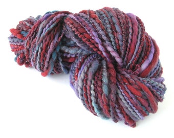 May include: A skein of yarn in shades of red, purple, and blue with silver metallic threads woven throughout.