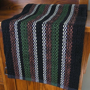 May include: A black table runner with stripes of green, brown, and white. The runner is woven with a textured pattern.