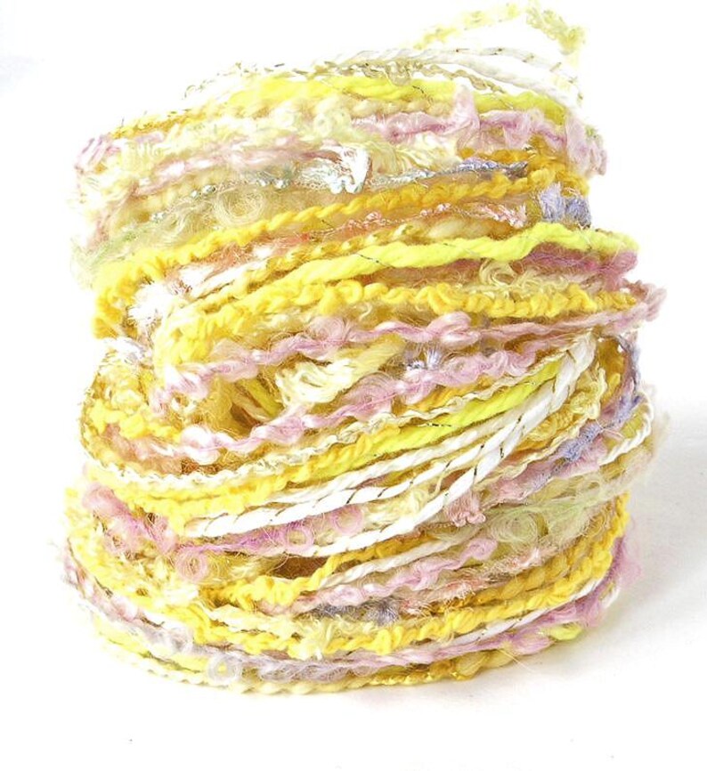 May include: A vibrant skein of yarn in shades of yellow, pink, and white. The yarn has a textured, multi-strand design with metallic silver accents. Ideal for knitting, crocheting, or other fiber art projects.