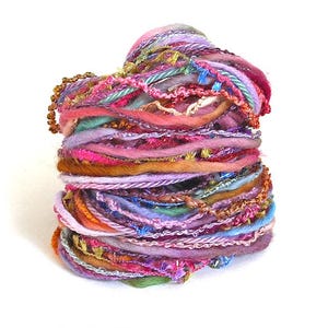 May include: A colorful, textured yarn ball composed of various threads in shades of pink, purple, orange, and green. The yarn features a mix of textures, including beaded strands and metallic threads, creating a visually rich and tactile appeal. Ideal for crafting projects.