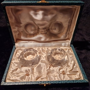 Op de afbeelding: Een vintage kristallen zout- en peperstel in een teal doos. De set bevat twee facetgeslepen kristallen zoutvaatjes en twee kleine lepels met goudkleurige accenten. De doos is gevoerd met satijn en heeft de tekst "Cristallerie Lorraine France".