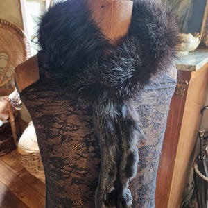 Peut inclure: Un col en fourrure noire avec un design long et fluide. Le col est présenté sur un mannequin avec une robe en dentelle noire. La fourrure semble douce et luxueuse, avec une couleur sombre et riche. C'est un accessoire vintage.